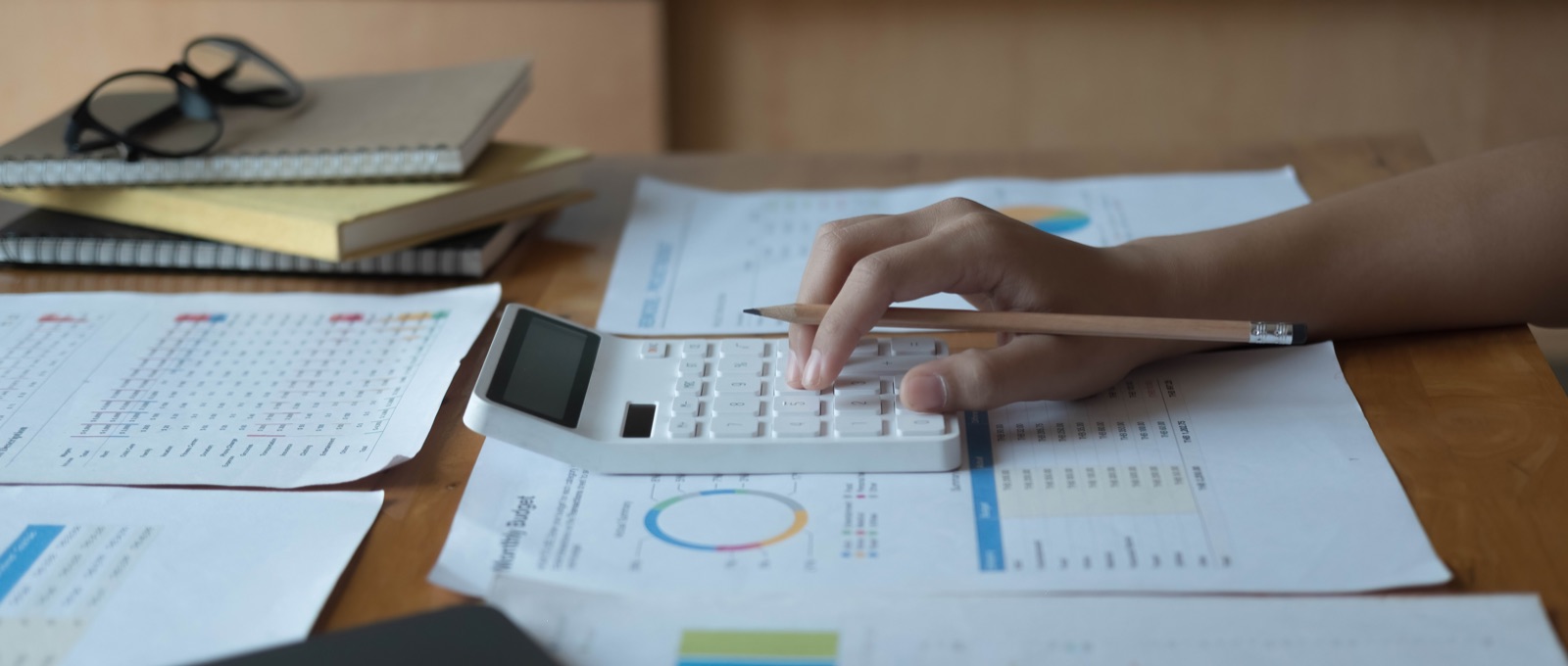 Budgeting by hand with a calculator, pencil, and printed spreadsheets on a desk